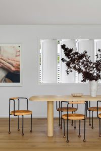 A modern Queenslander dining room with a large vase of dark leaves in the middle of the dining table.