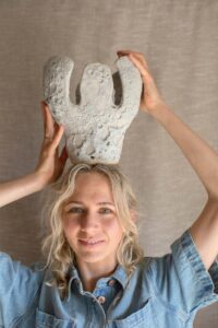 Ceramic artist Tess Miller holds a textured vase that she made on his head.