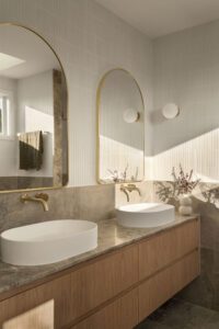 A modern architectural bathroom with brass finishings, marble bench tops, and oak cabinets.