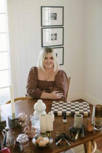 Photo of Hayley at home at her dining table, with props all over the table.