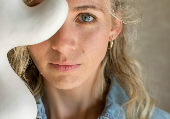 A close up of ceramic artist Tess Miller, one eye is covered by an organic shaped sculpture.